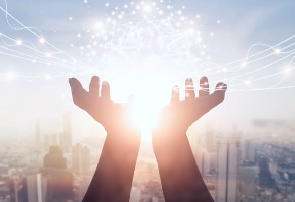 都市を背景に光を受ける手と未来的なエネルギーのイメージ